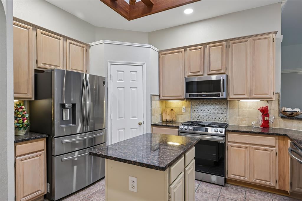 Kitchen featuring natural wood cabinetry, granite countertops, central island, stainless steel appliance suite, large pantry and tiled backsplash