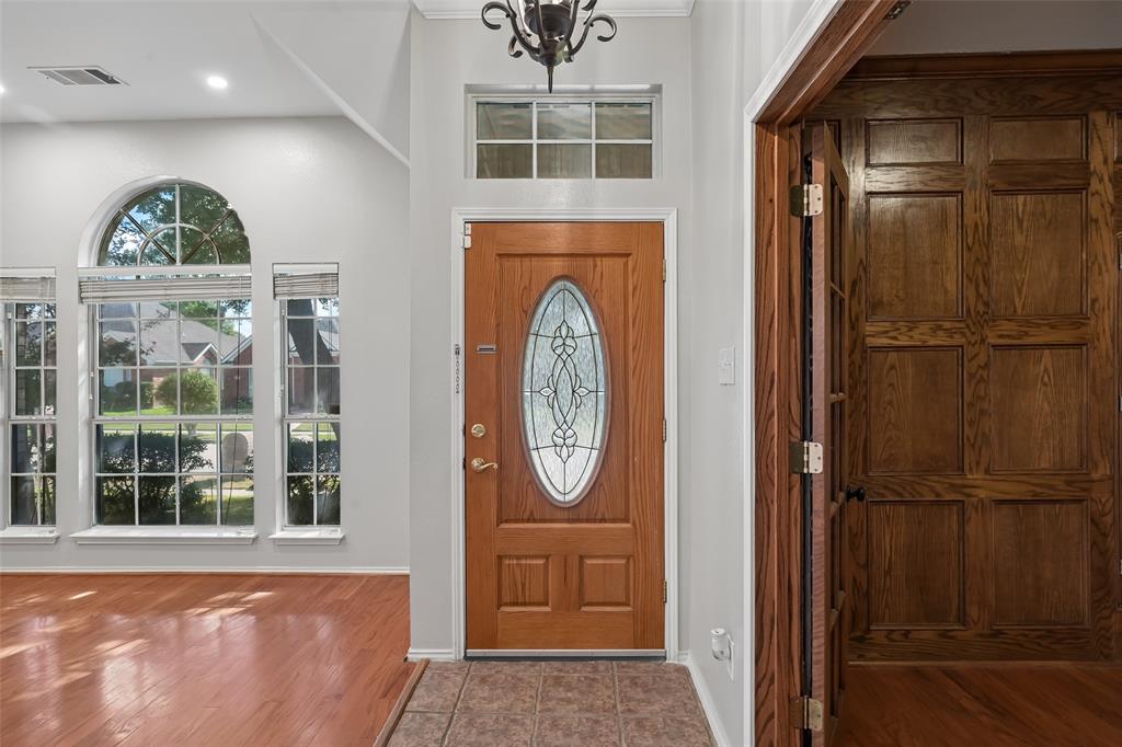 Entryway featuring a wood door with an oval decorative glass insert, wood-finish flooring, tile flooring, wall-mounted wood paneling, and large multi-pane windows with arched detailing