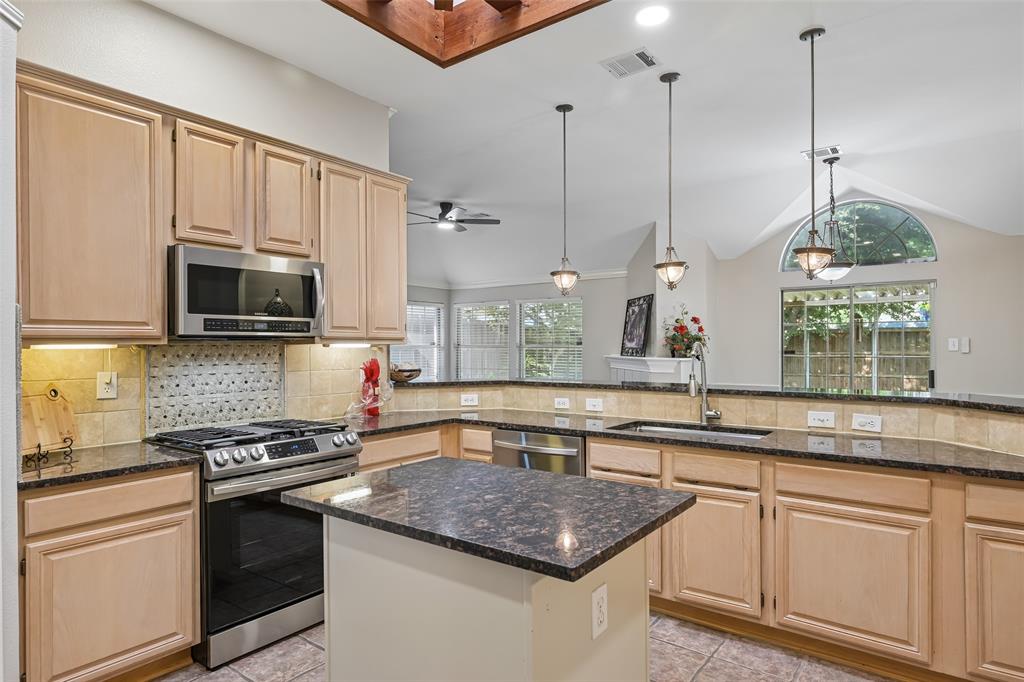 Kitchen featuring natural wood cabinetry, dark stone countertops, stainless steel appliances, a central island, and a decorative tile backsplash