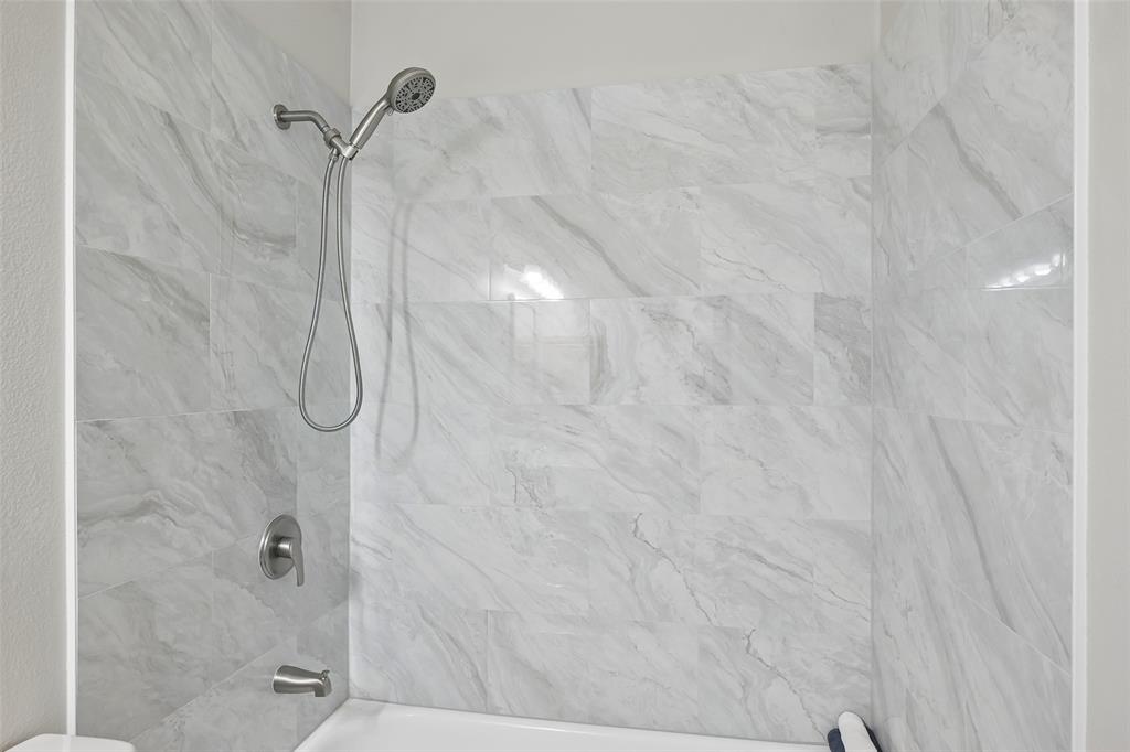 Shower enclosure featuring large-format stone-finish tile surround, brushed nickel finish handheld showerhead, matching single-handle pressure balance valve, and tub spout