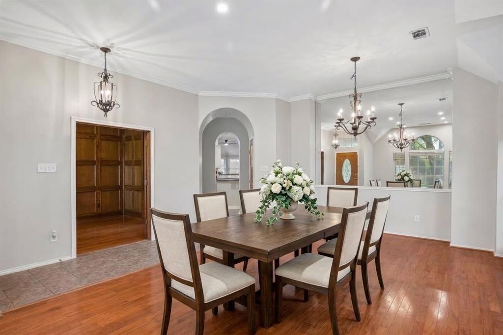 Interior space featuring wood-finish flooring, two decorative iron chandeliers, a large built-in mirror, an arched entryway, and wood-paneled walls