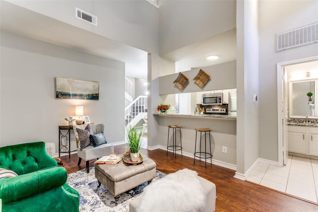 High-ceilinged living area featuring wood-finish flooring, a pass-through breakfast bar with stone-surface countertop, and a built-in staircase