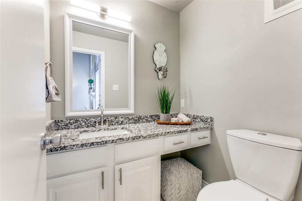 Bathroom vanity featuring a speckled stone-finish countertop, integrated rectangular sink, white cabinetry with brushed-metal pulls, and a framed wall-mounted mirror with overhead lighting
