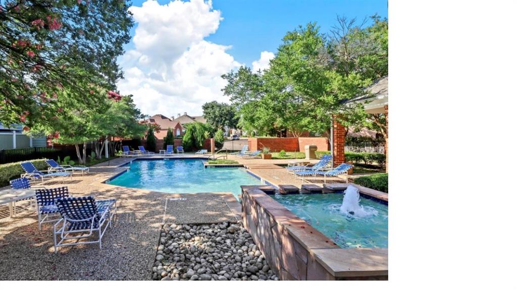 Outdoor pool area featuring a stone-clad spa with a fountain feature, pebbled hardscaping, masonry perimeter wall, and mature landscaping