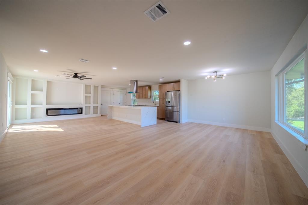 Open-concept interior featuring light wood-finish flooring, recessed lighting, built-in wall cabinetry, a stone-surround fireplace, and a kitchen island with a waterfall-edge countertop