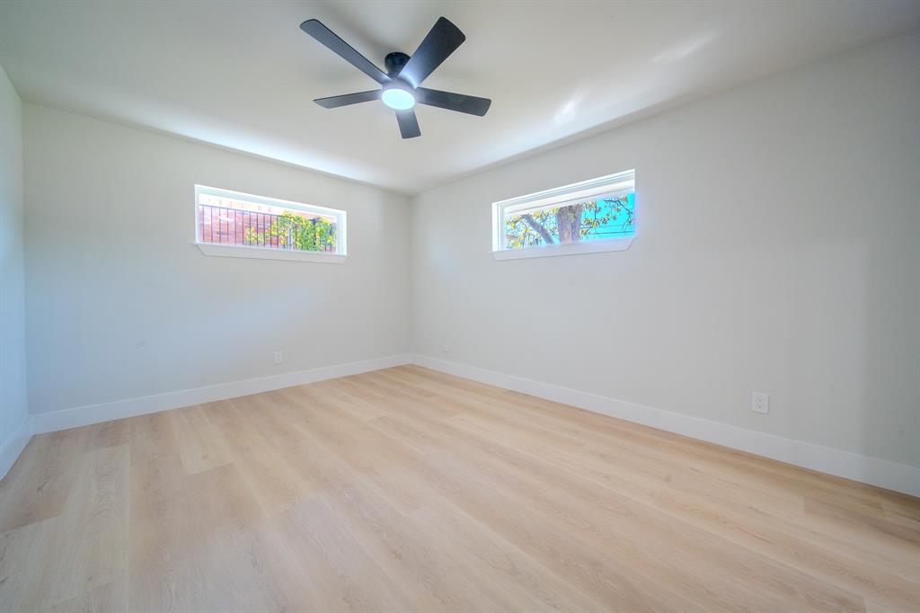 Neutral-toned interior room featuring wood-finish flooring, two horizontal rectangular windows, and a matte black ceiling fan with an integrated light fixture