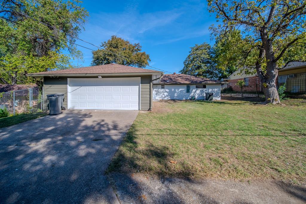 Exterior featuring a detached garage with horizontal siding, concrete driveway, and expansive lawn with mature trees