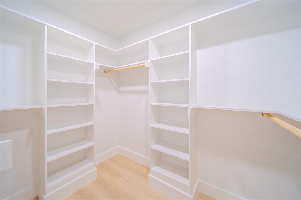 Custom walk-in closet featuring white built-in shelving, wooden hanging rods, and wood-finish flooring