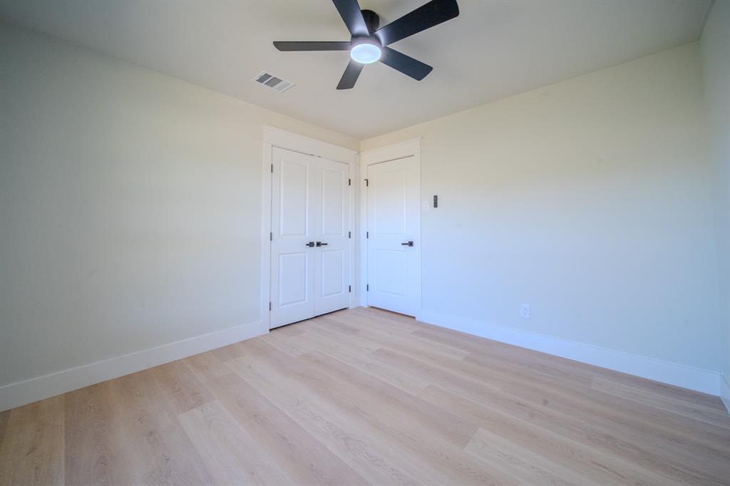 Light-toned wood-finish flooring, matte black hardware, dual-panel interior doors, and a modern ceiling fan with integrated lighting