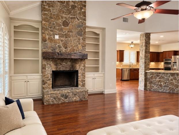 Floor-to-ceiling stone fireplace with a timber mantel, flanked by custom built-in cabinetry, hardwood flooring, vaulted ceilings, and Plantation Shutters!