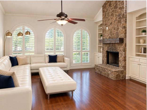 Floor-to-ceiling stone fireplace with a timber mantel, flanked by custom built-in cabinetry, hardwood flooring, vaulted ceilings, and Plantation Shutters!