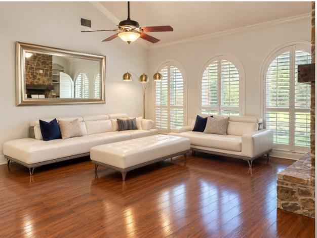Floor-to-ceiling stone fireplace with a timber mantel, flanked by custom built-in cabinetry, hardwood flooring, vaulted ceilings, and Plantation Shutters!