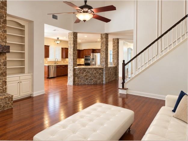 Floor-to-ceiling stone fireplace with a timber mantel, flanked by custom built-in cabinetry, hardwood flooring, vaulted ceilings, and Plantation Shutters! Open to Kitchen.
