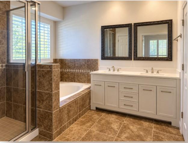 New Dual-sink vanity with a solid-surface countertop, tile-surrounded soaking tub, glass-enclosed shower, and tile flooring.