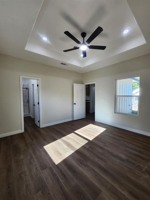 Tray ceiling featuring recessed lighting and a central ceiling fan, paired with wood-finish flooring