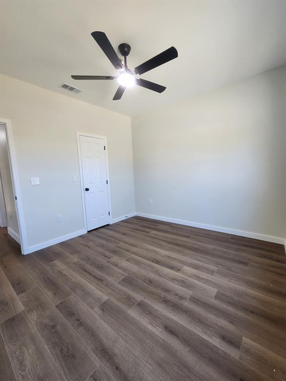 Room featuring wood-finish flooring, a five-blade ceiling fan, and a six-panel door Room featuring wood-finish flooring, a five-blade ceiling fan, and a six-panel door