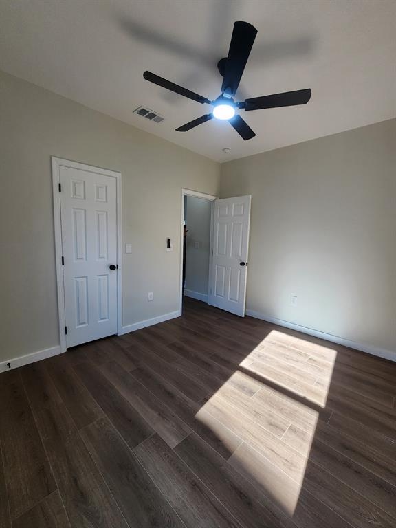 Neutral-toned interior featuring wood-finish flooring, two six-panel interior doors, and a ceiling-mounted fan with an integrated light fixture