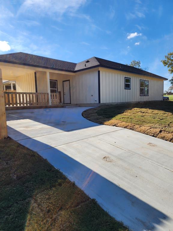 Board-and-batten siding exterior featuring a concrete driveway, attached carport with wooden railing, and dark-tone roof shingles