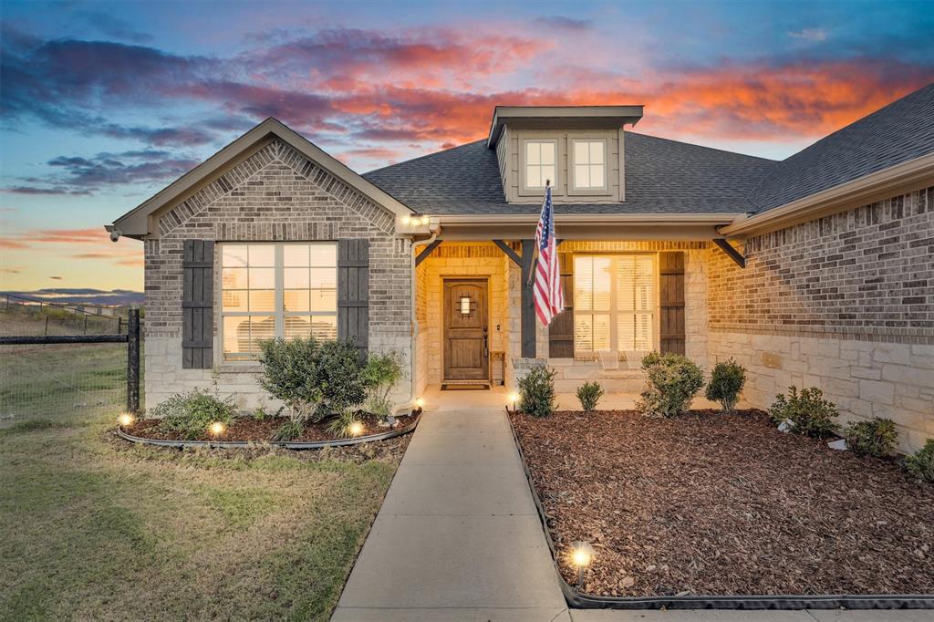 Brick and stone exterior featuring dark wood-finish shutters, a covered entryway, and a dormer window
