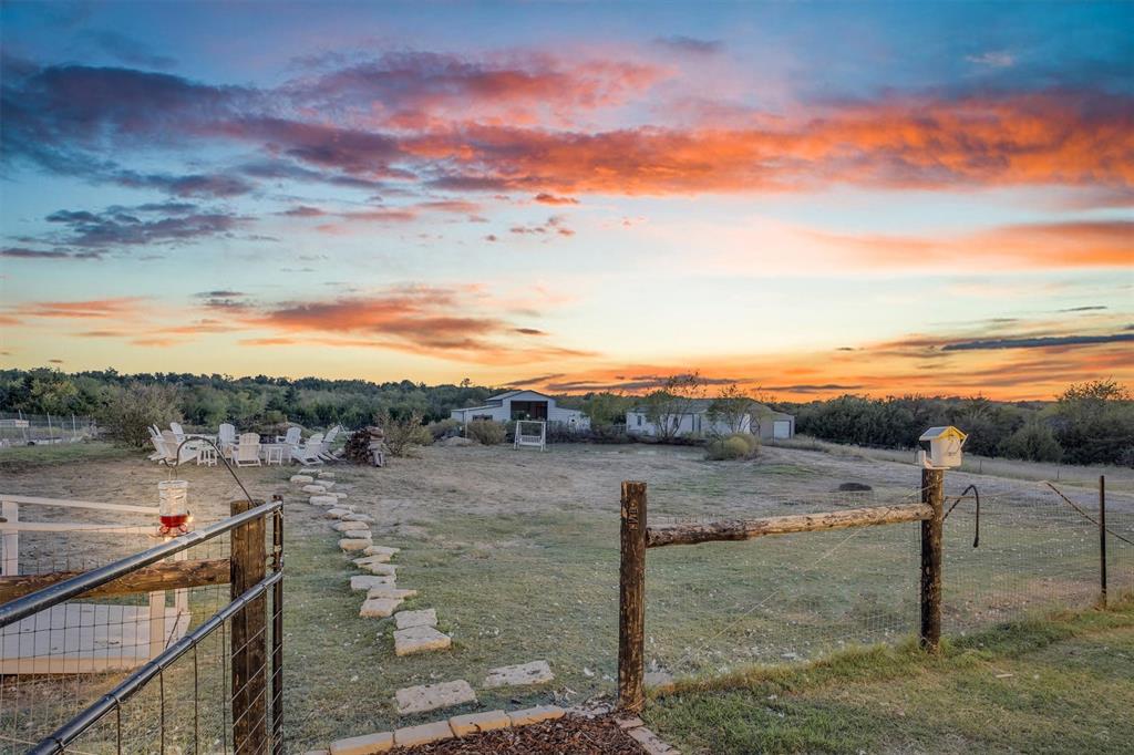 Expansive grounds featuring a stone paver path, wooden post-and-rail fencing, and outbuildings against a prominent sunset horizon