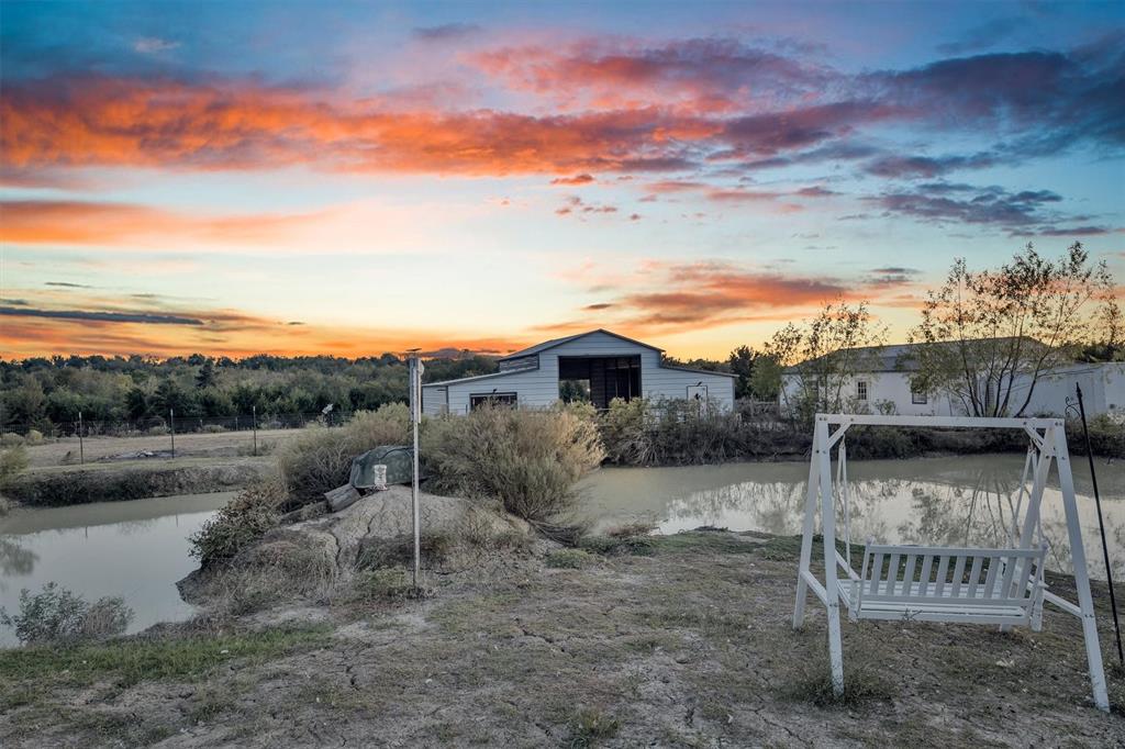 Rural property featuring a pond, outbuilding, and expansive horizon at sunset