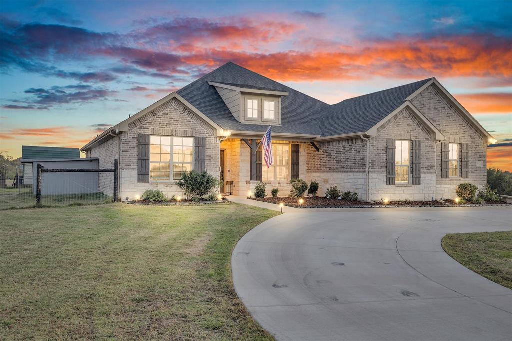 Multi-gabled brick and stone facade featuring decorative window shutters, a covered entryway with timber support beams, and a curved concrete driveway