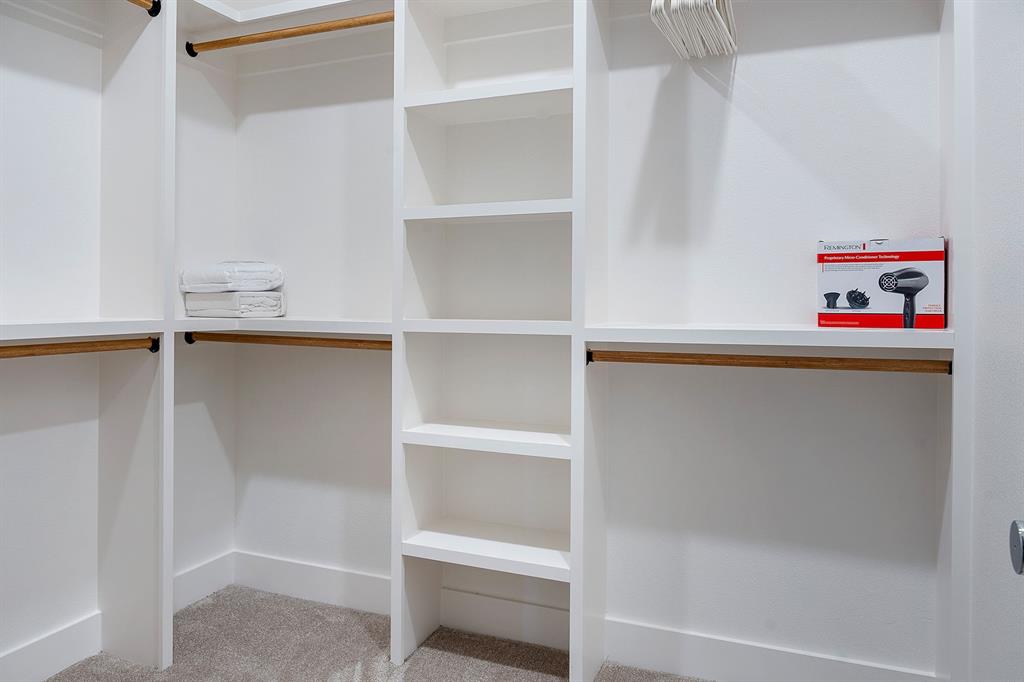 Walk-in closet featuring white built-in shelving, multiple hanging rods, and neutral carpeting