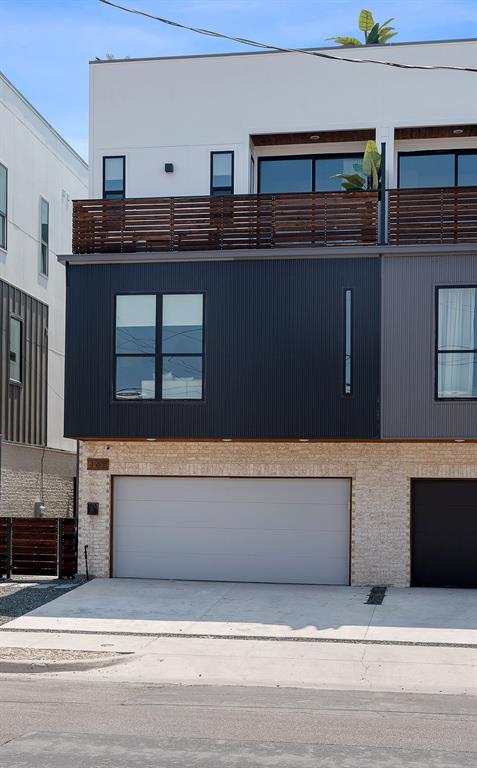 Modern multi-level exterior featuring white stucco, black vertical siding, light-toned stone masonry, horizontal wood-slat balcony railings, and a concrete driveway