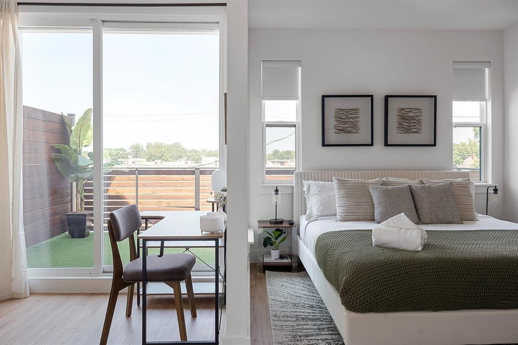 Sliding glass doors opening to a private balcony with horizontal wood slat fencing and artificial turf, complemented by wood-finish flooring and dual double-pane windows