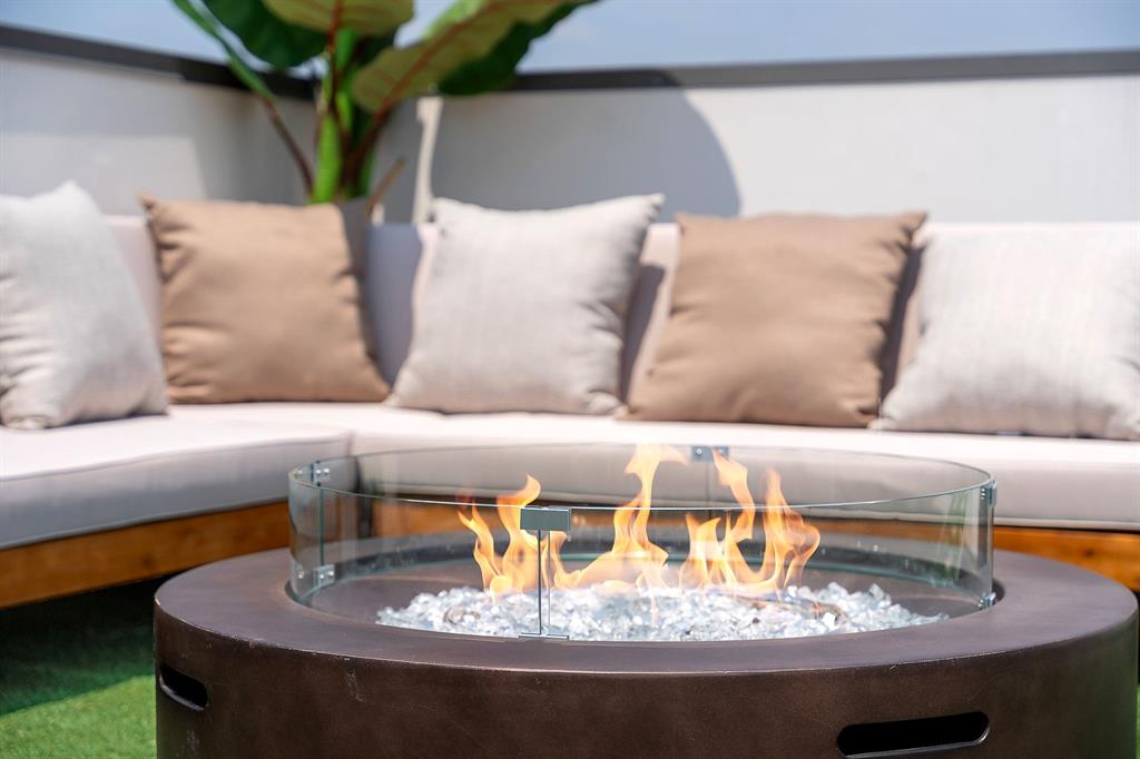Circular fire pit featuring a smooth dark-toned base, integrated glass wind guard, and decorative stone filler