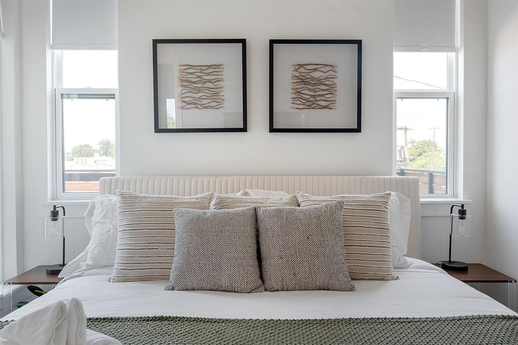 Dual vertical windows with roller shades, complemented by wall-mounted lighting fixtures on fixed wooden bedside platforms