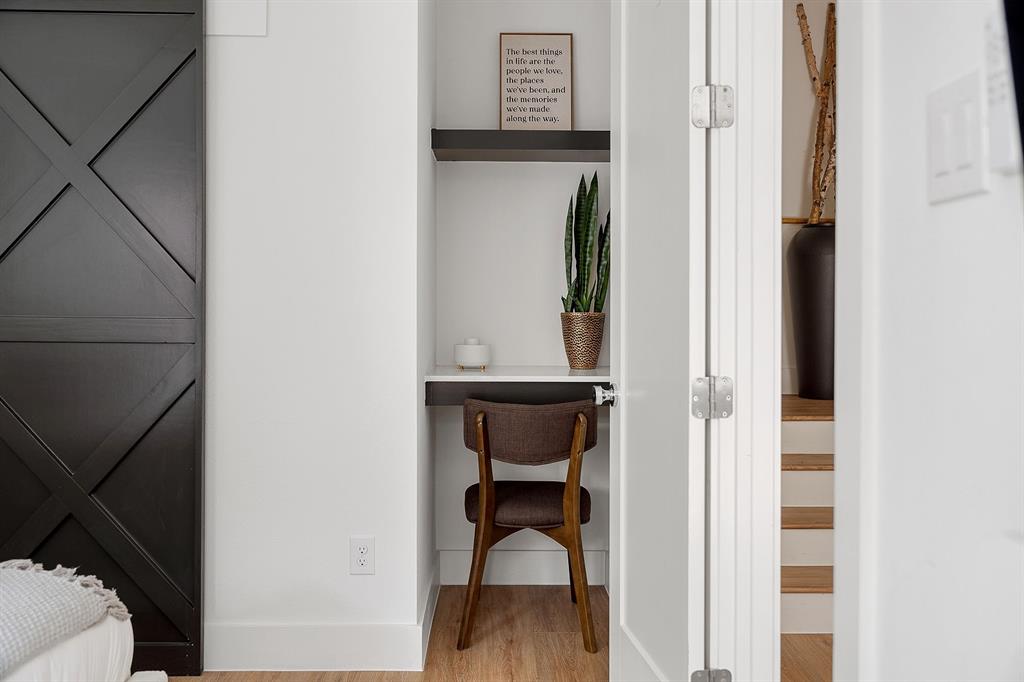 Built-in alcove featuring a floating desk, overhead shelving, wood-finish flooring, and a sliding barn-style door with a cross-brace design
