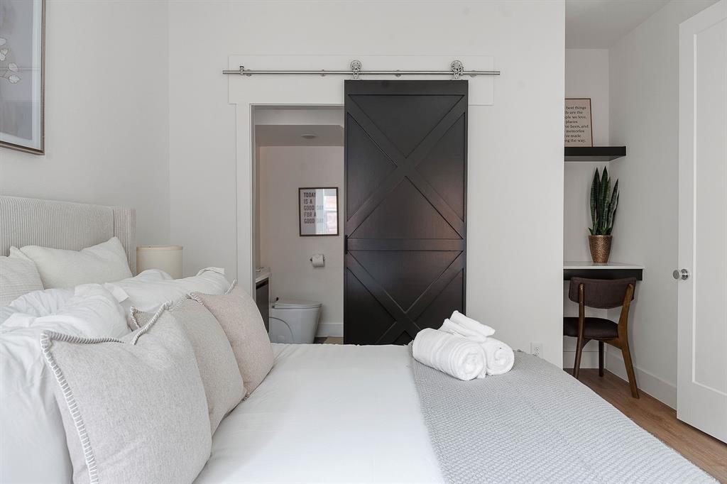 Dark-finished X-pattern sliding barn door with brushed metal hardware, built-in floating desk with stone surface, and wood-finish flooring