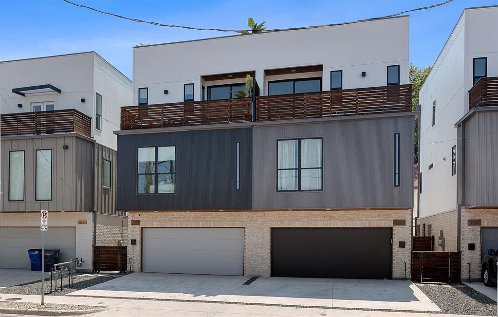 Modern multi-story exterior featuring a stone veneer base, mixed-material metal siding, wood-slat balcony railings, and dual garage access Modern multi-story exterior featuring a stone veneer base, mixed-material metal siding, wood-slat balcony railings, and dual garage access