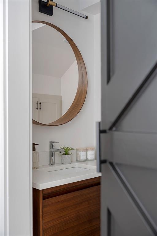 Modern vanity with a wood-finish cabinet, rectangular integrated sink, circular wood-frame mirror, matte black wall-mounted vanity light, and charcoal-toned sliding door