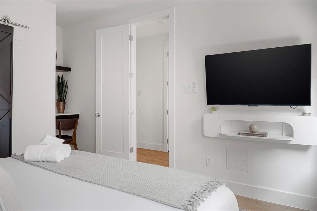 Dark wood-finish sliding barn door, wall-mounted white media console with integrated shelving, recessed desk nook with floating shelf, and solid-core interior doors featuring brushed nickel hardware