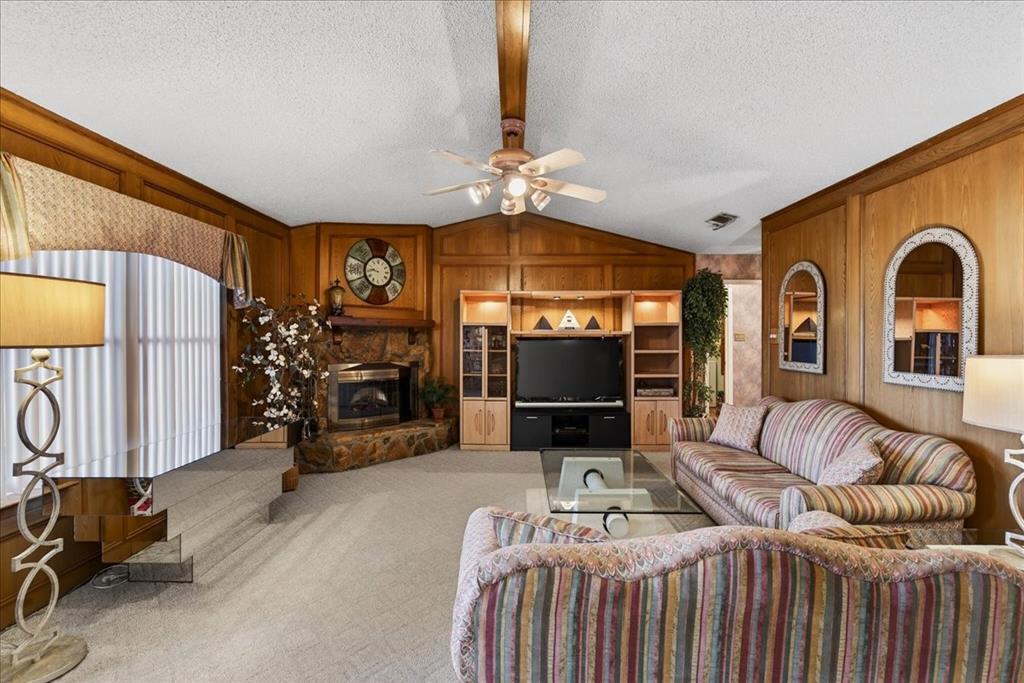 Vaulted ceilings with a central ceiling fan, wood-paneled walls, stone-faced fireplace, and built-in media cabinetry
