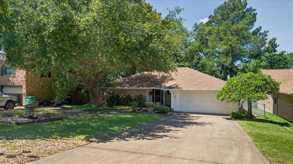 Single-story brick exterior featuring an attached two-car garage, concrete driveway, and mature trees