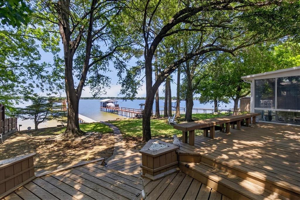 Multi-level wood deck featuring built-in bench seating, a stone-accented fire feature, mature trees, and a private dock extending into the water