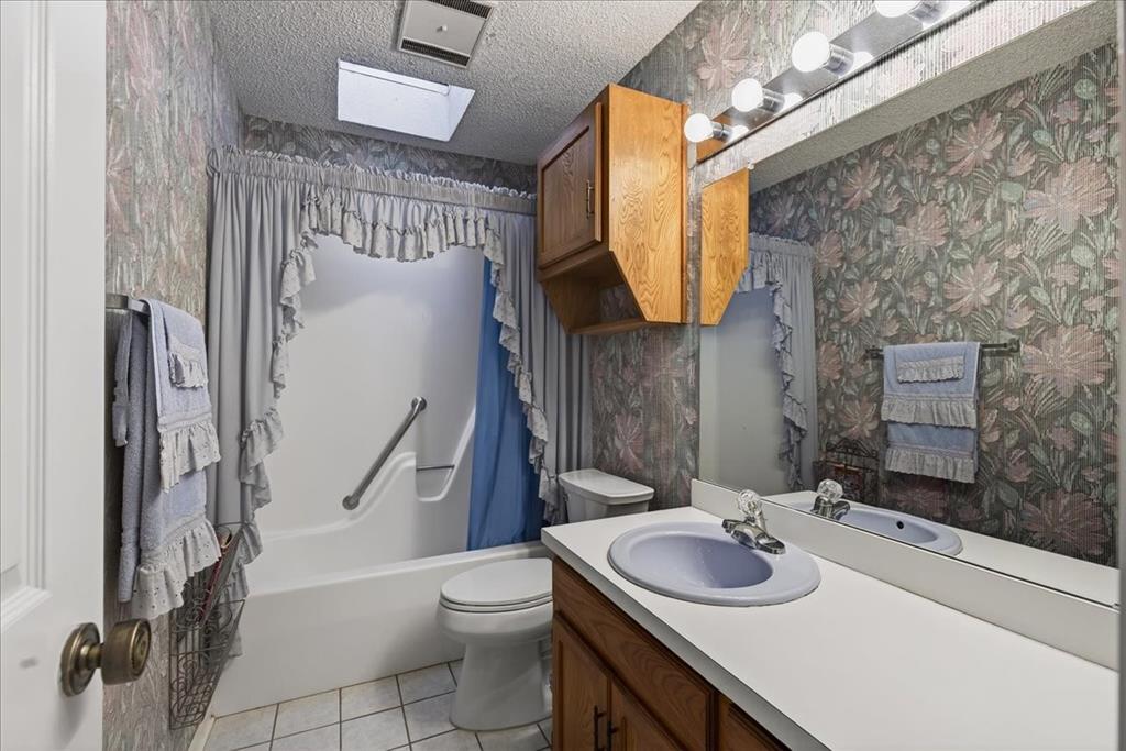 Bathroom featuring a skylight, wood cabinetry, a vanity with an integrated basin, and a combination tub and shower enclosure with a stainless steel grab bar