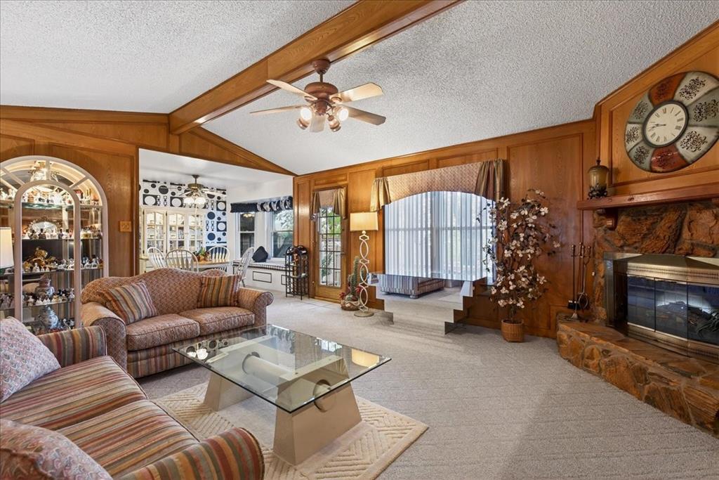 Vaulted ceilings featuring exposed wooden beams, natural stone fireplace with a wooden mantel, wood-paneled walls, and built-in arched display cabinetry