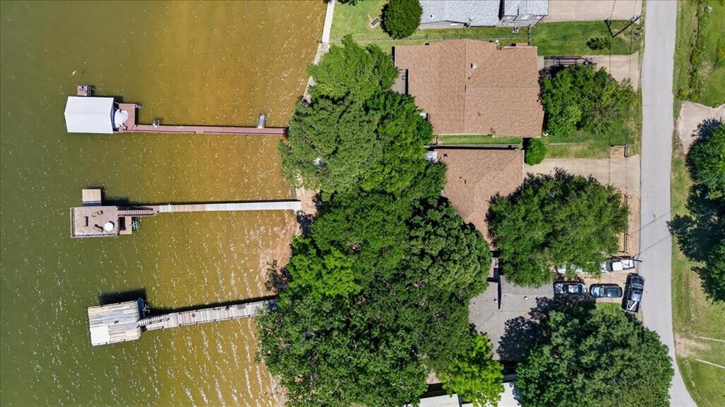 Aerial perspective of waterfront property featuring three private docks, extensive shoreline, mature trees, and paved surface parking