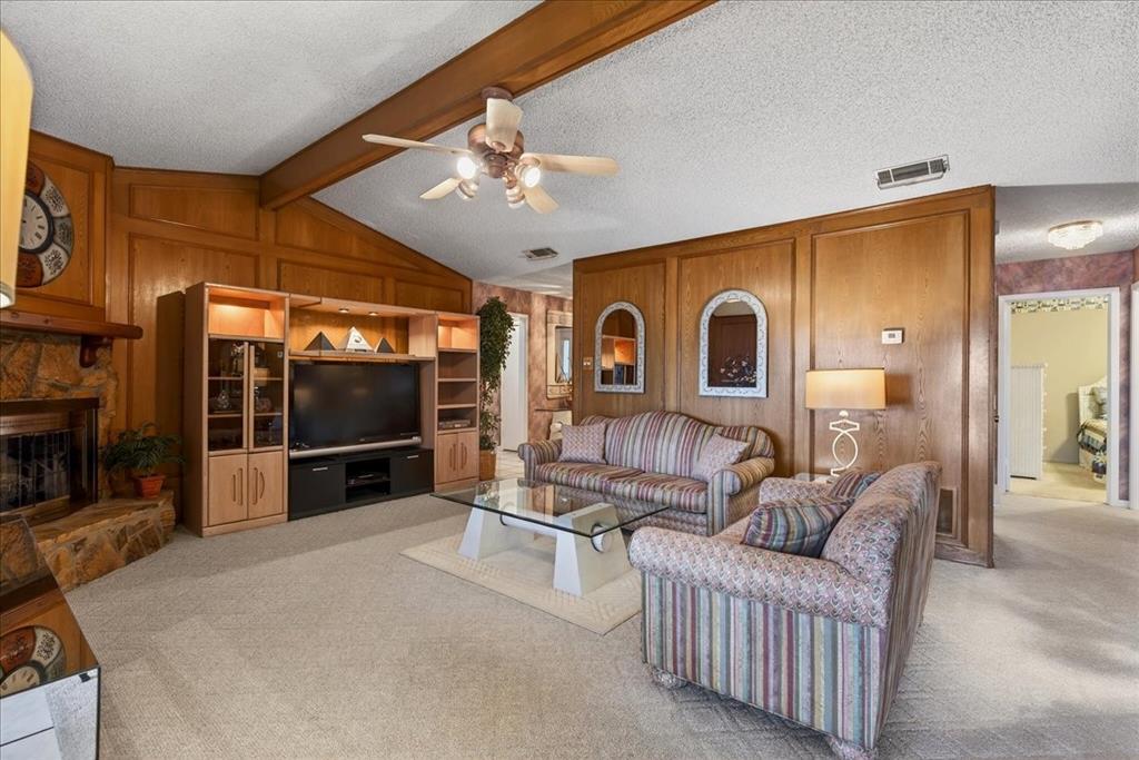 Living room featuring vaulted ceilings with exposed wood beams, wood-paneled walls, a stone-surround fireplace, and custom built-in cabinetry
