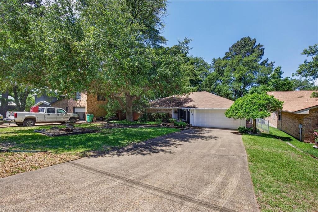 Single-story brick exterior featuring a concrete driveway, two-car garage, and mature trees