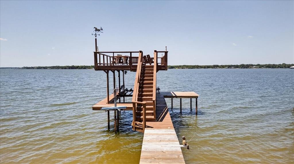 Multi-level wooden dock featuring an upper observation deck, staircase with railings, boat lift, and metal weather vane