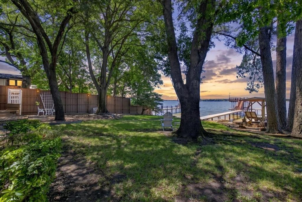 Lakeside grounds featuring mature trees, a wooden privacy fence, and a private dock