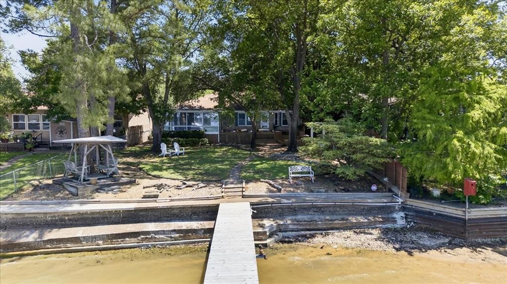 Waterfront property featuring a private wooden pier, tiered stone bulkheading, mature trees, and a landscaped yard