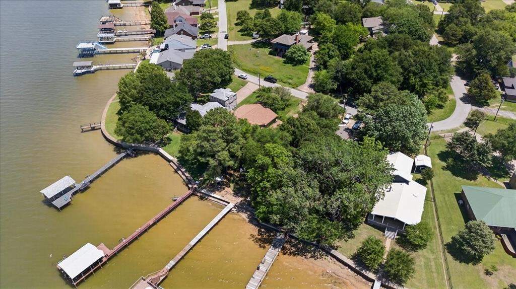 Aerial perspective of waterfront property featuring a private boat dock, natural shoreline, mature trees, and paved access