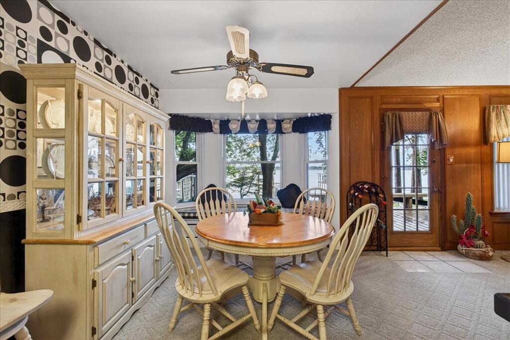 Dining area featuring a built-in floor-to-ceiling hutch, bay windows, wood-paneled walls, a glass-paneled exterior door, and a ceiling fan with integrated lighting