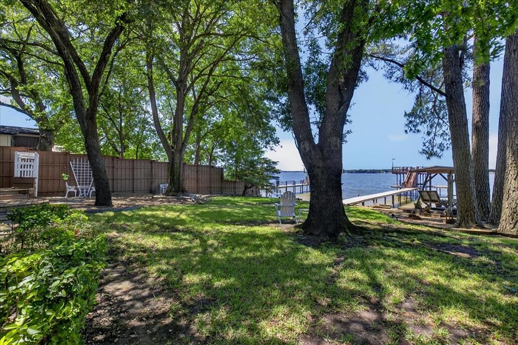 Waterfront property featuring mature trees, a private dock, and a wood privacy fence
